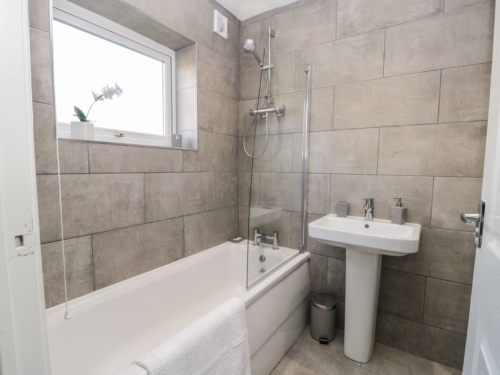 A bathroom with a bathtub shower combination a pedestal sink and a window with a plant at Araucaria House in Whitby