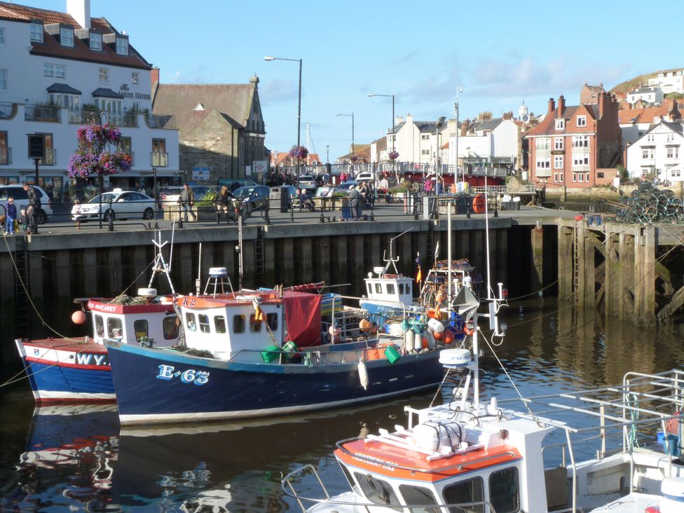Fishing boats docked in a harbor with people walking along the quay and buildings in the background at Araucaria House in Whitby
