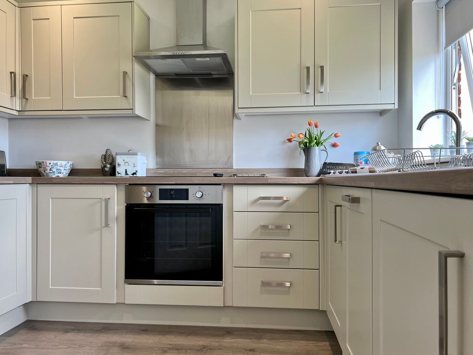 A kitchen with white cabinets oven stovetop wooden countertop and a vase with flowers at Araucaria House in Whitby