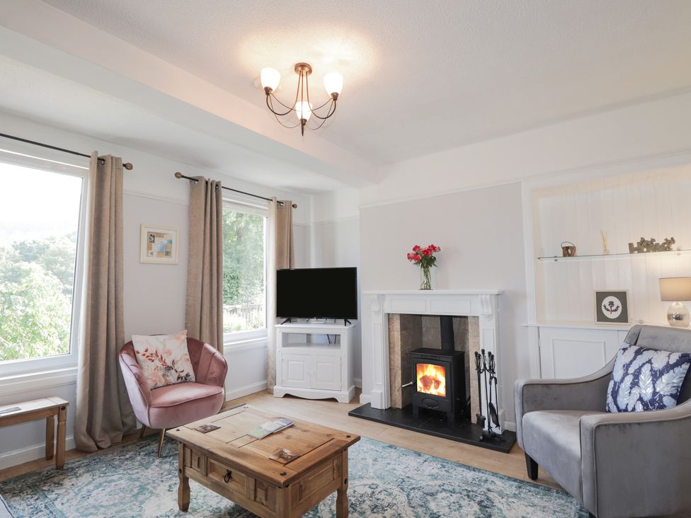 A living room with a fireplace television armchairs a coffee table and windows at 2 Riverside in Foyers