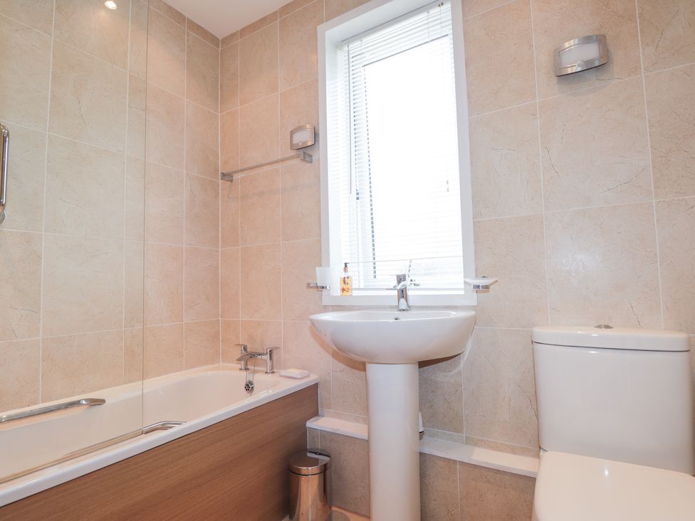 A bathroom with a bathtub, pedestal sink, toilet, and window with blinds at 2 Riverside in Foyers