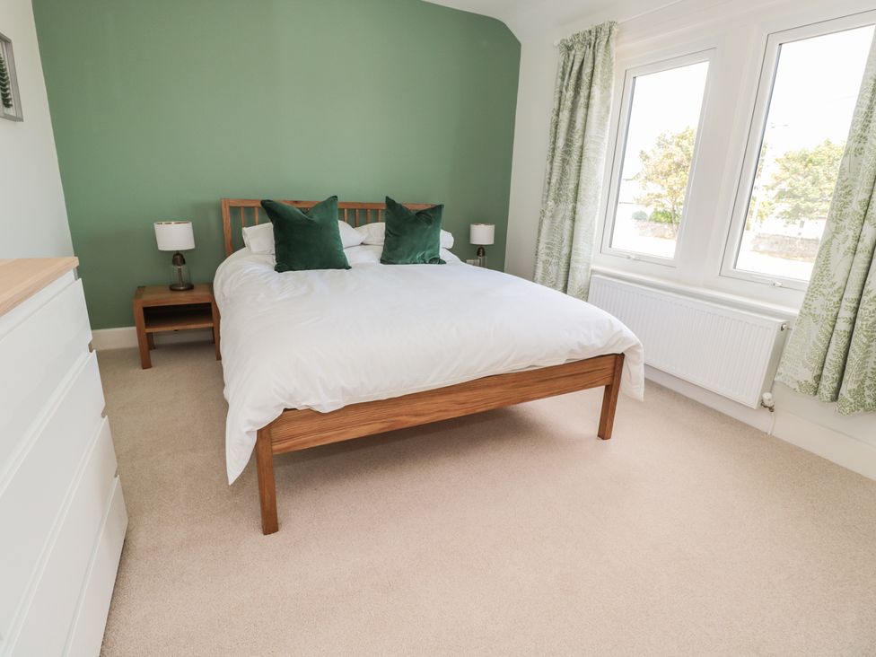 A bedroom with a wooden bed with white bedding and green pillows bedside tables with lamps and a white chest of drawers at 60 King Street in Seahouses