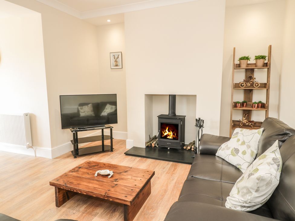 A living room with a TV on a stand a wood stove a wooden coffee table and a sofa at 60 King Street in Seahouses