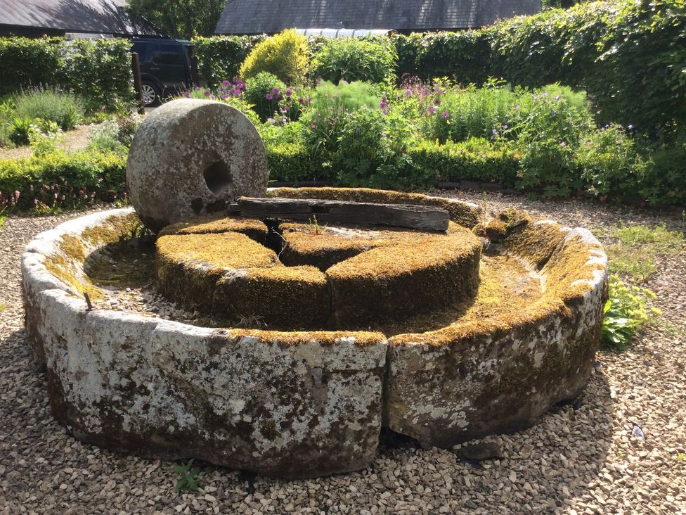 An old stone mill wheel covered in moss in a garden with flowers and bushes at The Granary in Eardisley
