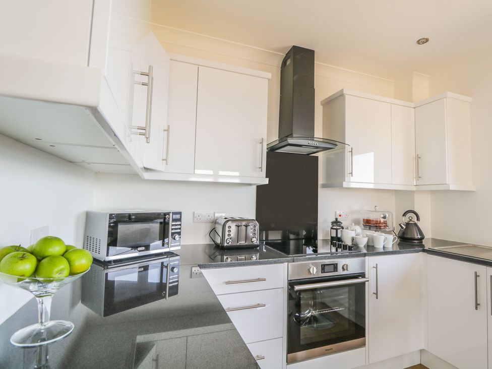 A kitchen with white cabinets black countertop microwave toaster stove oven kettle and a bowl of green apples at 24 Waters Edge in Banff