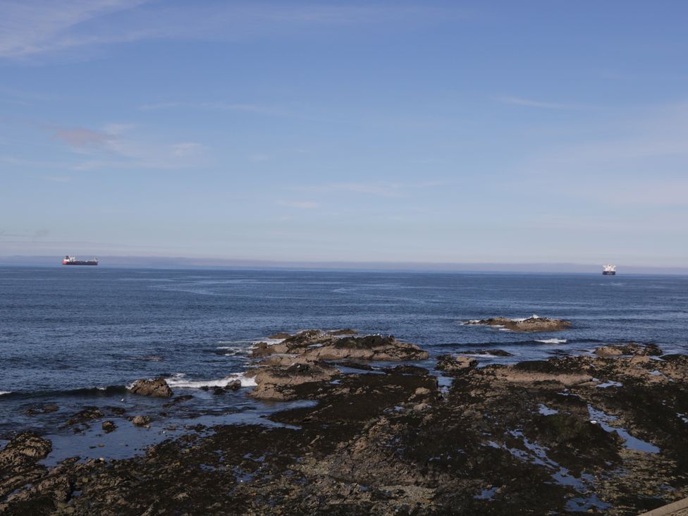 Rocky shoreline with two ships in the ocean and a clear sky at 24 Waters Edge in Banff