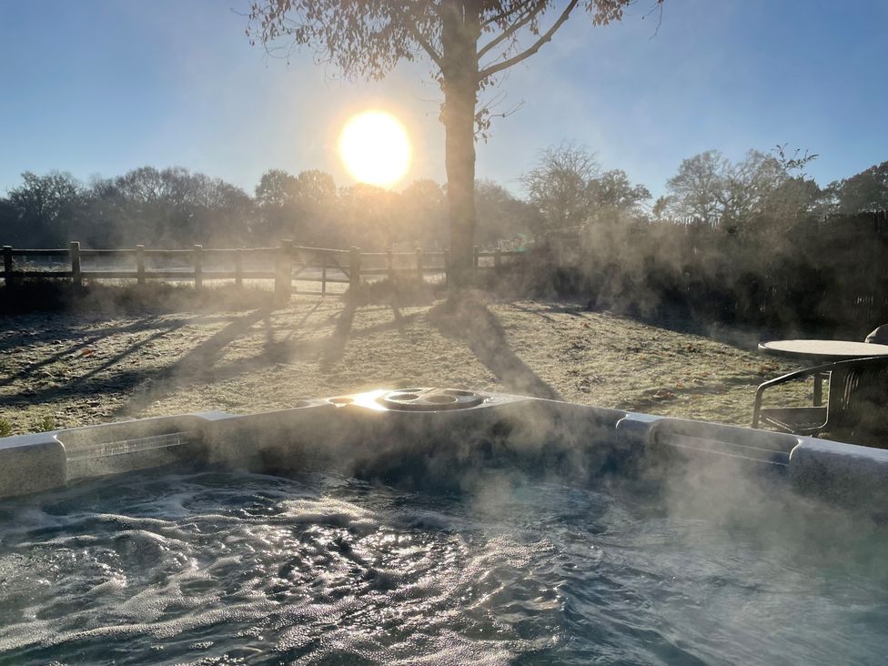 An outdoor hot tub with steam rising a tree and a fence in the background at Pheasant Lodge in Wimborne Minster