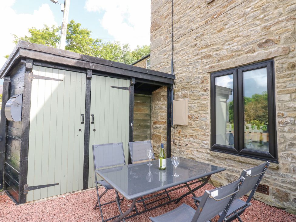 An outdoor seating area with a table glass bottle and three glasses next to a stone building and a wooden shed at Skovhaven in Catton