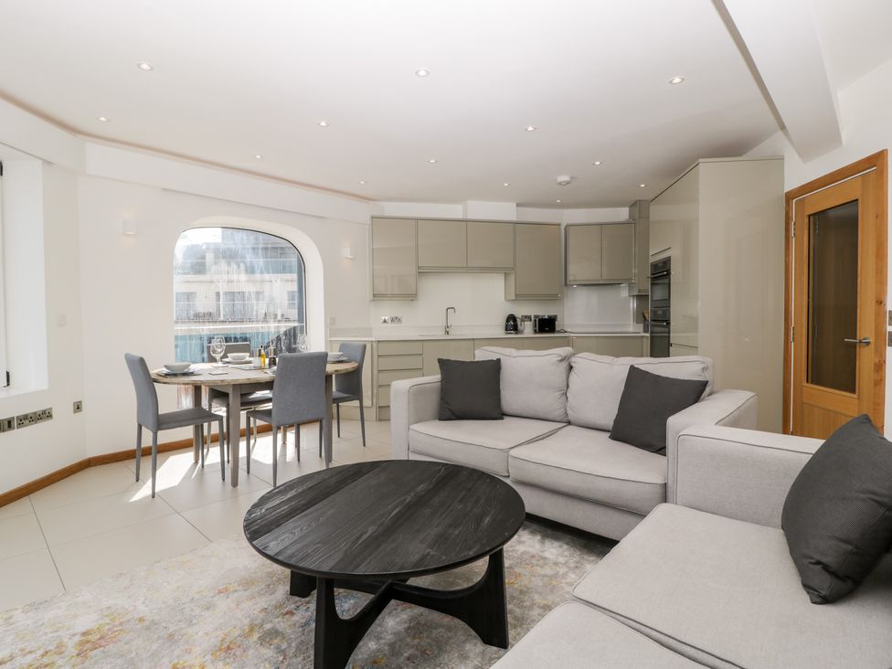 An open plan living room and kitchen with a round dining table and gray chairs at 1 Ocean Bay in Swanage