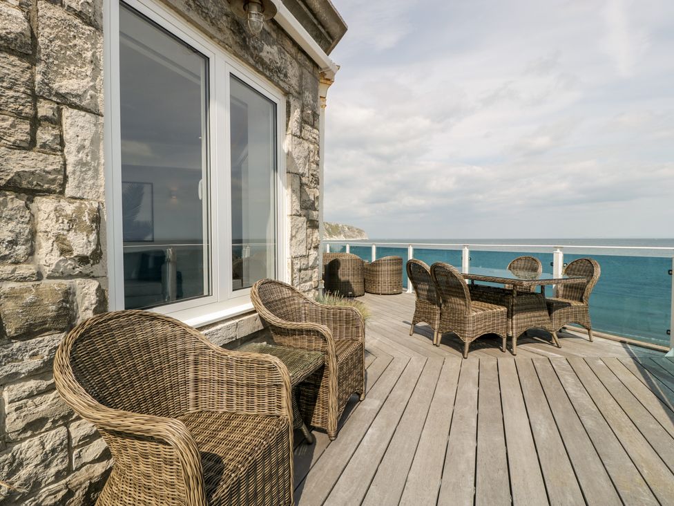 An outdoor deck with wicker chairs and a table overlooking the sea at 1 Ocean Bay in Swanage