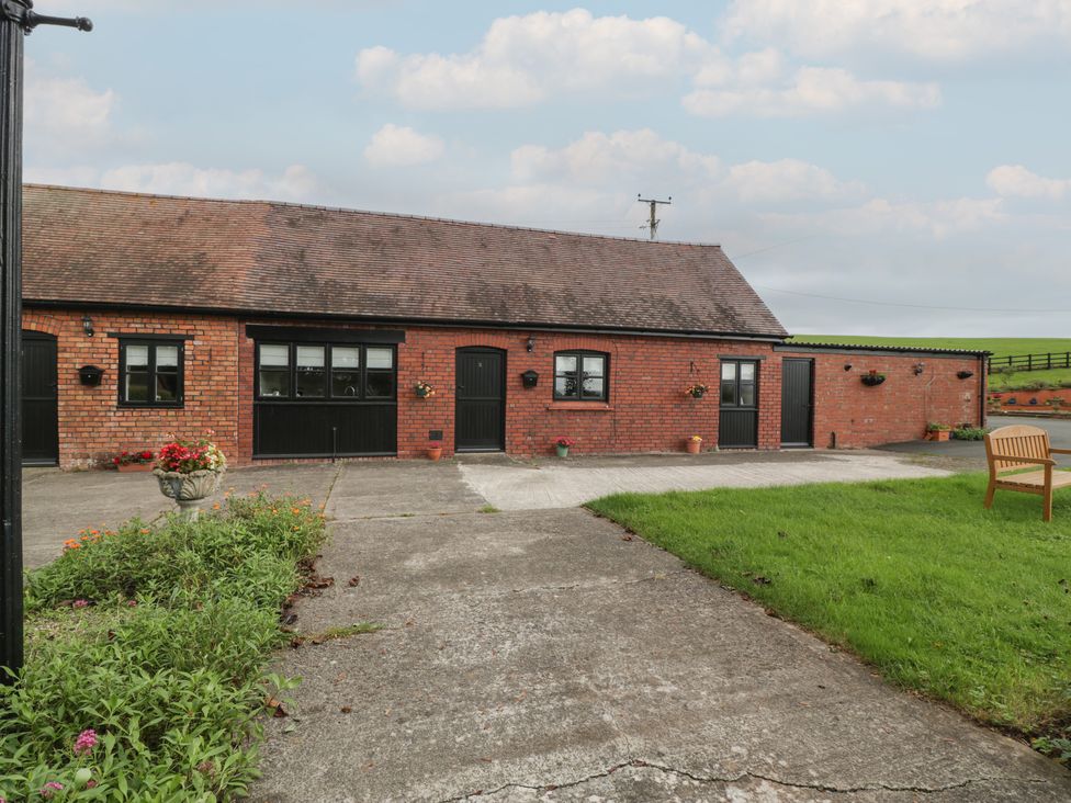 An exterior view of a brick building with multiple black doors and windows a paved walkway a grassy area and outdoor bench at The Pheasant Two in Raglan