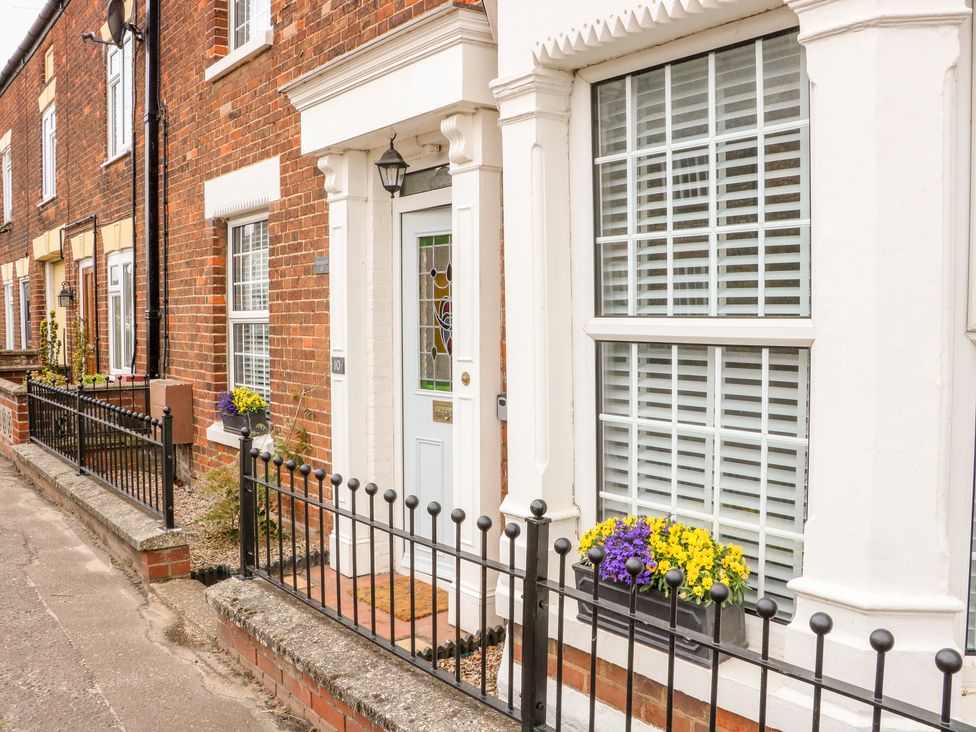 The exterior of a brick house with a white door and windows with flower boxes behind a black metal fence at Springfield in Hempton near Fakenham