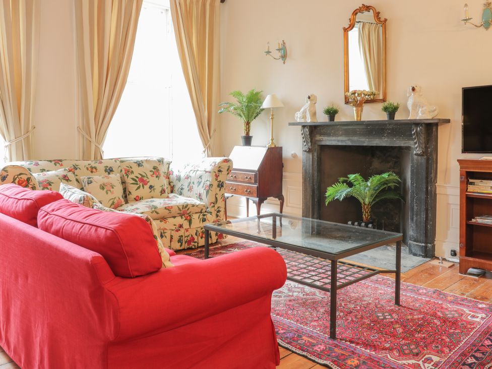 A living room with a red couch a floral couch a glass coffee table a fireplace with decor and a TV unit at 3 Lynedoch Place Edinburgh