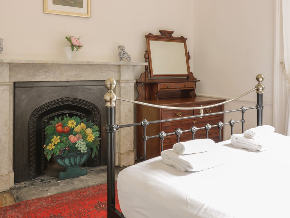 A bedroom with a metal bed frame white towels on the bed a wooden dresser with a mirror and a fireplace with a decorative screen at 3 Lynedoch Place in Edinburgh