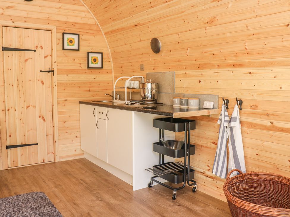 A kitchen area with wooden walls a white cabinet black countertop a metal pot and kettle a three-tier black trolley striped towels and a wicker basket at Dingle Den in Craswall