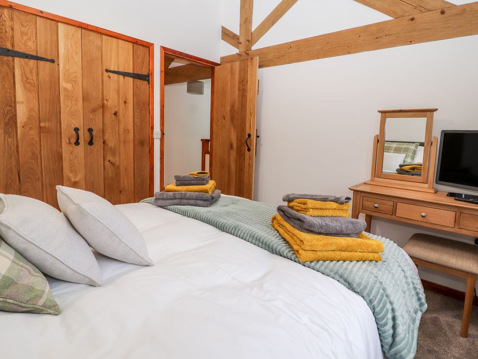 A bedroom with a bed folded towels wooden wardrobes and a dressing table with a mirror at The Old Cart House in Nantmawr near Trefonen