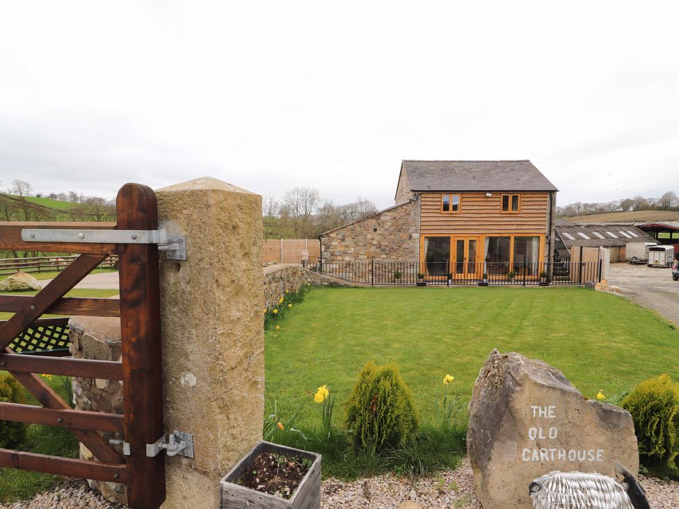 A stone and wood house with a fenced lawn and a wooden gate at The Old Cart House in Nantmawr near Trefonen