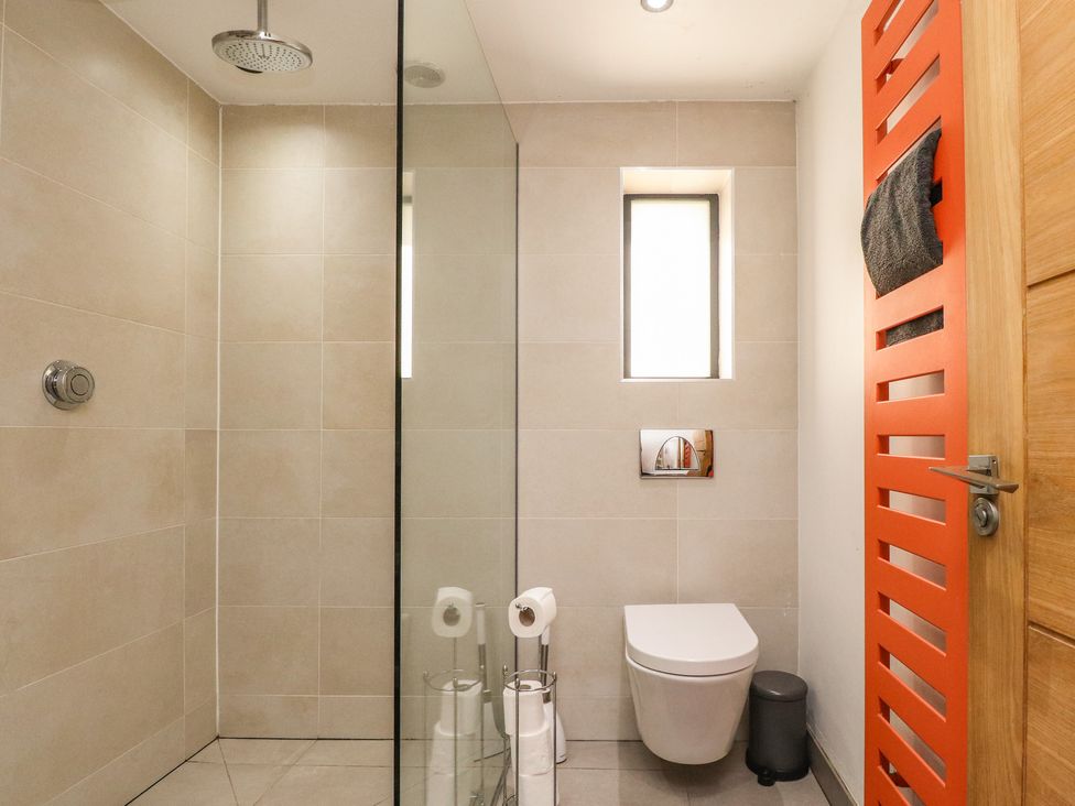 A bathroom with a shower area glass divider wall white toilet window and orange towel rack at Underfell in Burton-In-Kendal