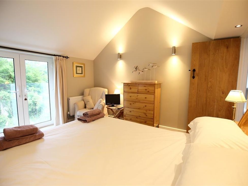 A bedroom with a bed folded towels a wooden dresser an armchair and glass doors at The Cottage in St Briavels