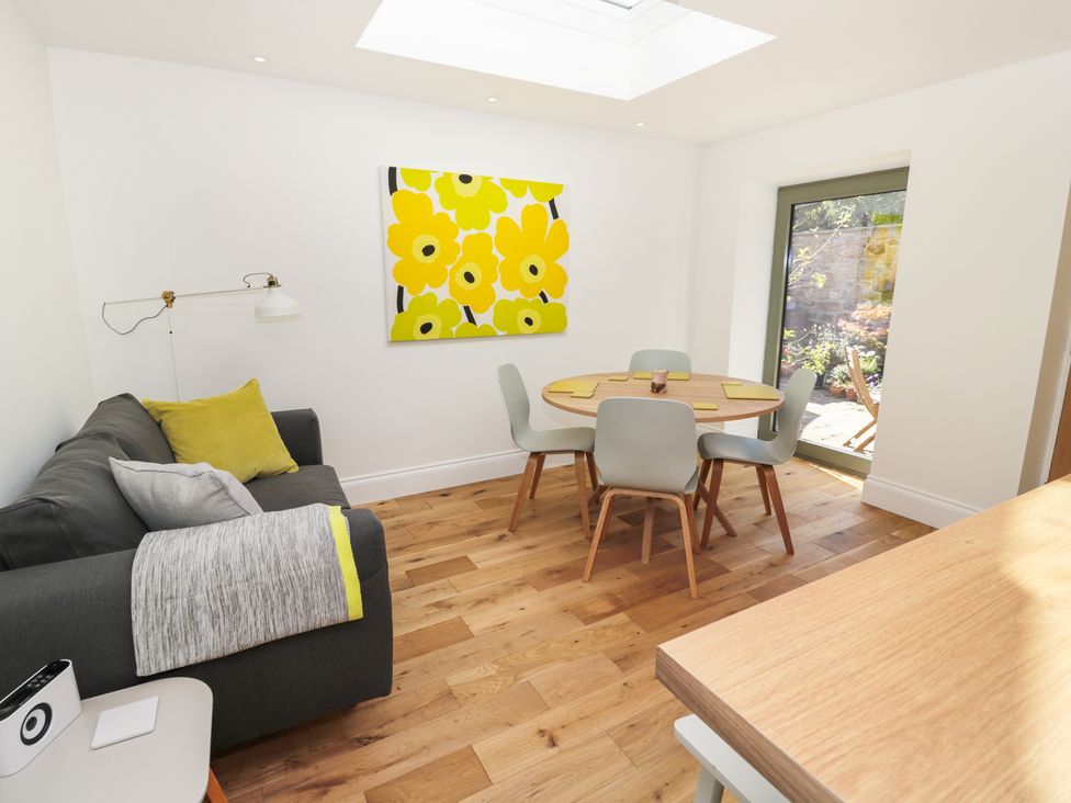 A dining area with a round table and four chairs next to a sofa with cushions and a wall painting at Teviot Cottage in Corbridge