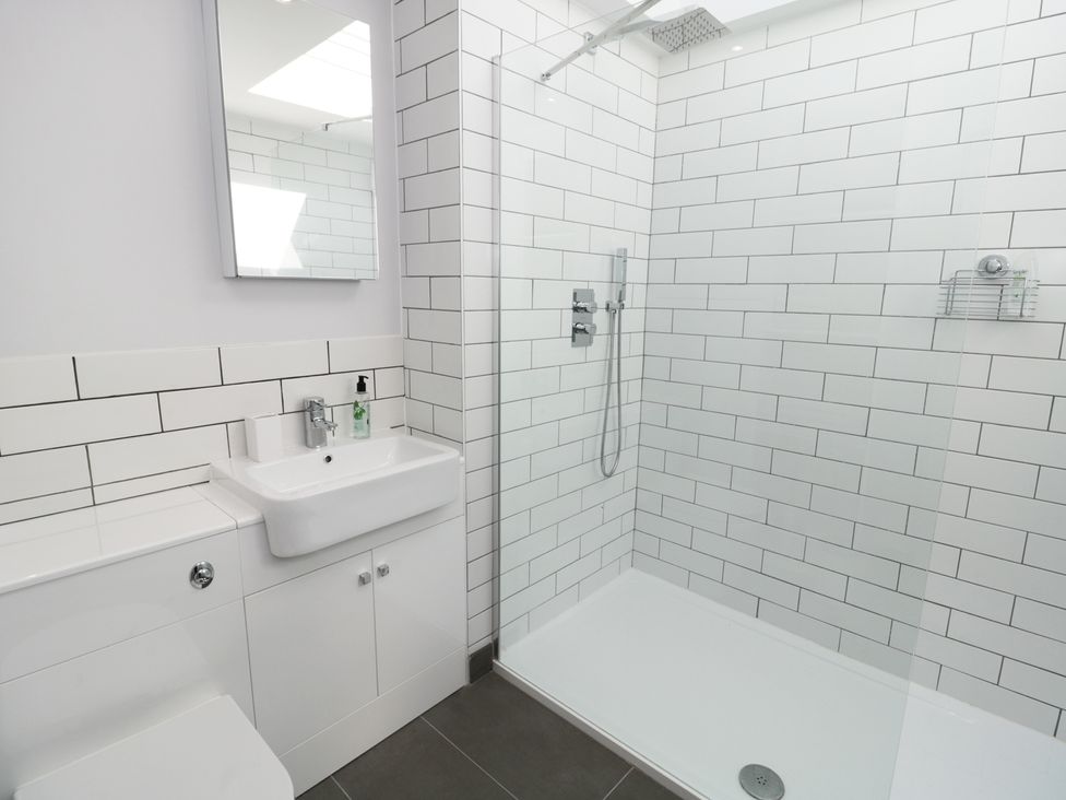 A bathroom with a sink, mirror, toilet, and shower area with white tiled walls at Teviot Cottage in Corbridge