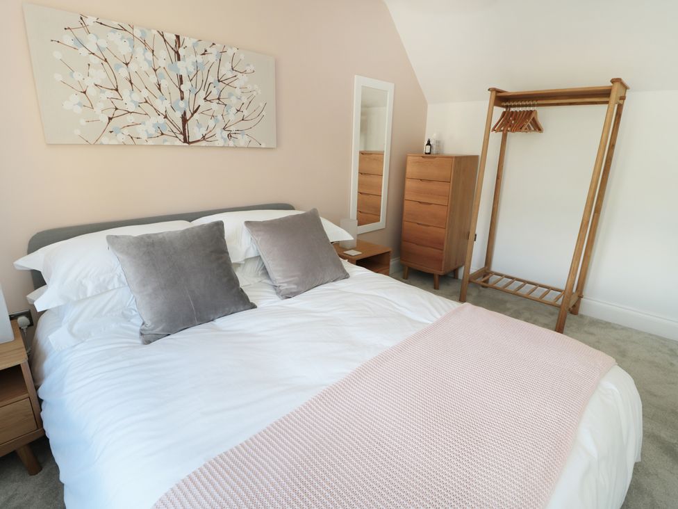 A bedroom with a bed with white bedding and grey pillows a wooden chest of drawers a mirror and a wooden clothes rack at Teviot Cottage in Corbridge