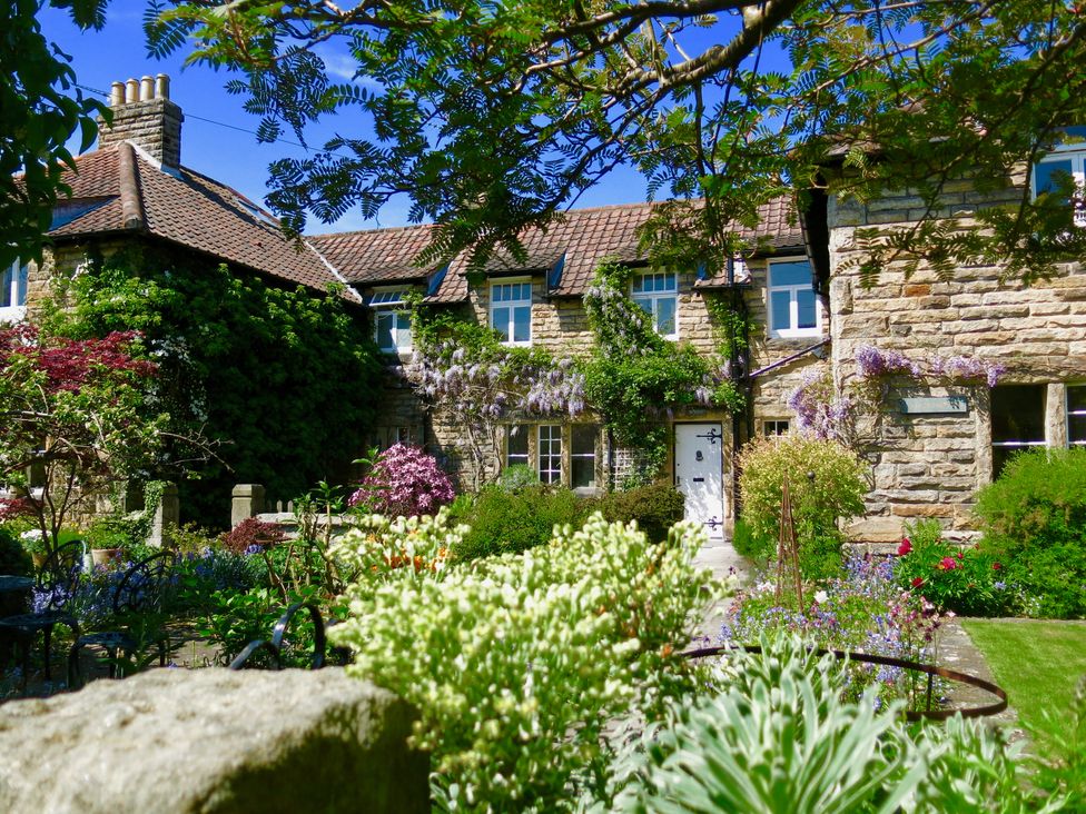 A stone cottage with a tiled roof surrounded by a garden with various plants and flowers at Teviot Cottage in Corbridge