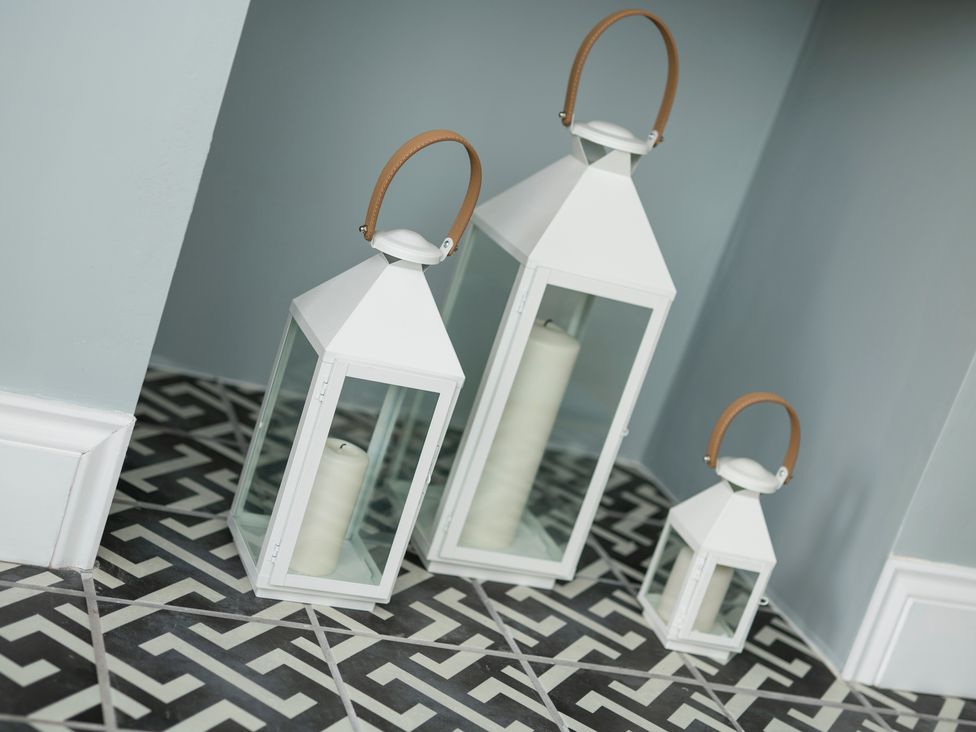 Three white lanterns with candles inside on a patterned floor at Teviot Cottage in Corbridge