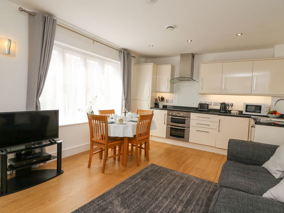 A kitchen and dining area with a table set for four wooden chairs a television on a stand and a grey sofa at Admiral's Quarter Apartment 4 in Weymouth