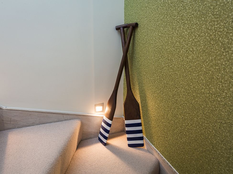 Two wooden oars with striped blades resting on carpeted stairs against a wall at Villa 8 Estura in Salcombe