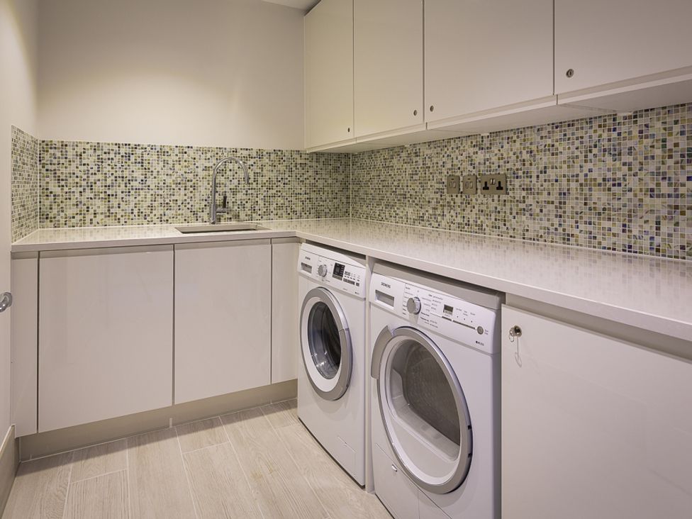 A laundry room with washing machines under a countertop and mosaic tiled backsplash at Villa 8 Estura Salcombe