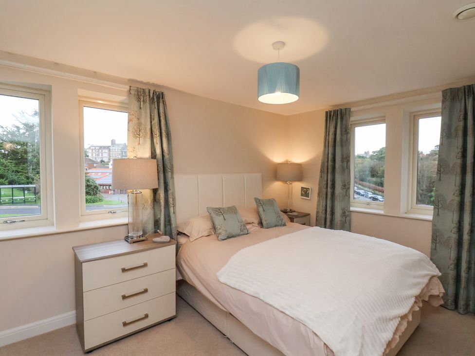 A bedroom with a bed between two nightstands and windows with curtains at Time and Tide Apartment 25 in Whitby