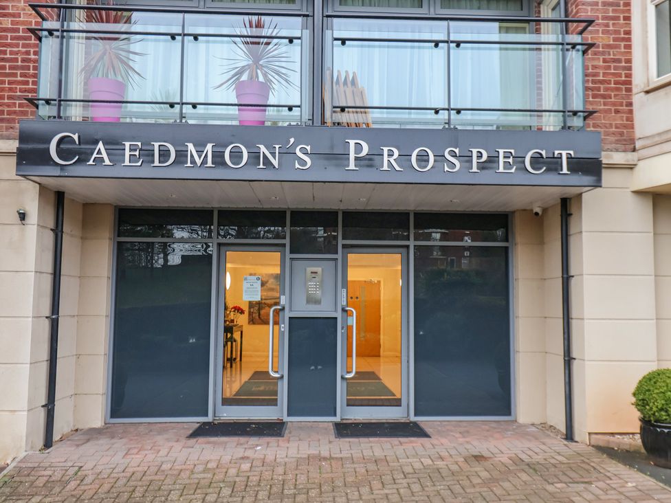 Entrance to a building with glass doors under a sign that reads Caedmon's Prospect with a balcony above the entrance